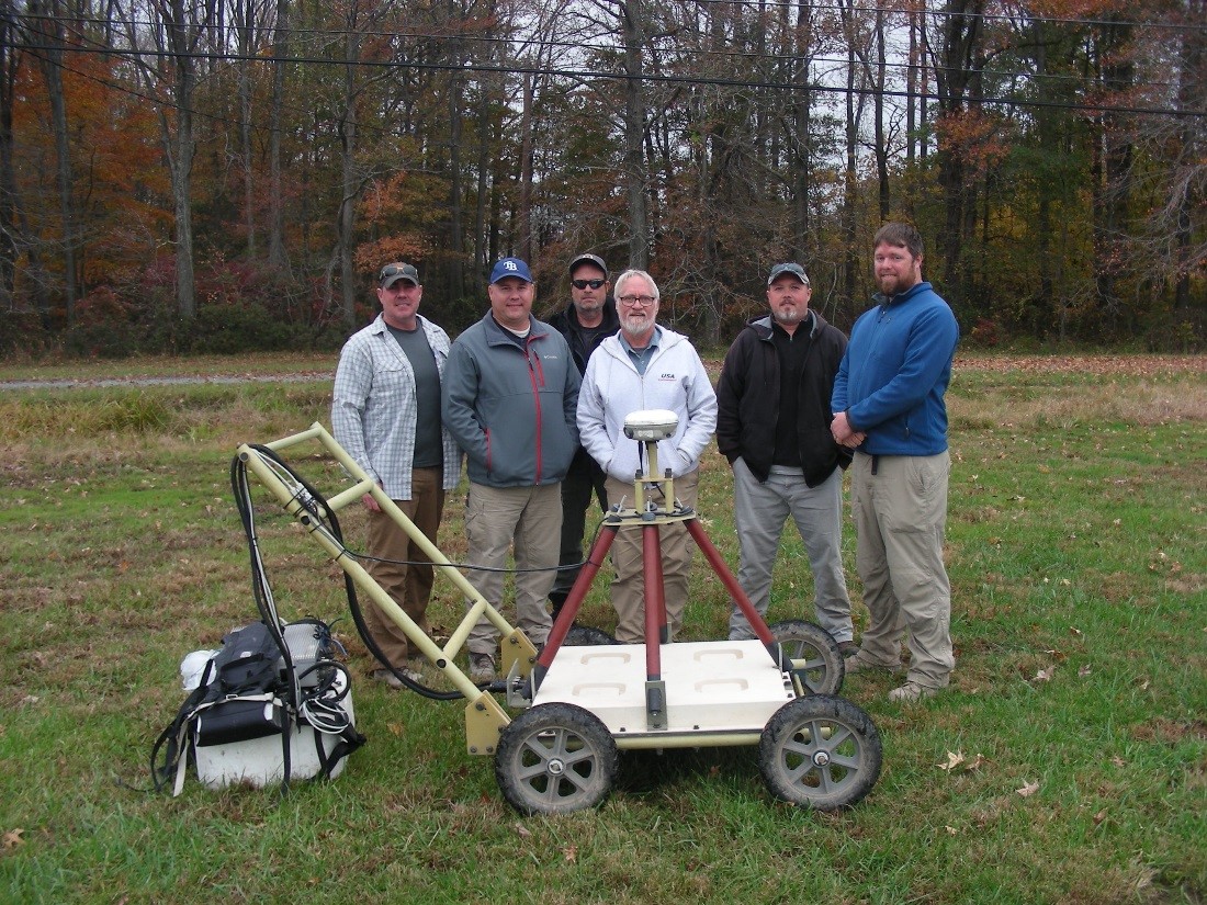 Caption: (pictured left-right) Ric MacNeil, Jeff Lewis, Ted Pate, Al Crandall, Allen Cochran and Scott Crandall stand behind a cart-mounted Time Domain Electrometric Multi-sensor Towed Array Detection System (TEMTADS) 2x2x3. 